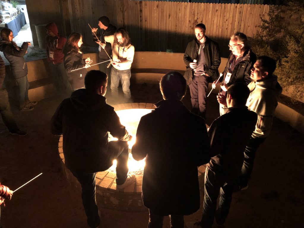 A group of developers huddles around a firepit with marshmallows on sticks