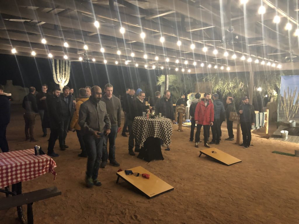 Developers play cornhole under a well lit awning